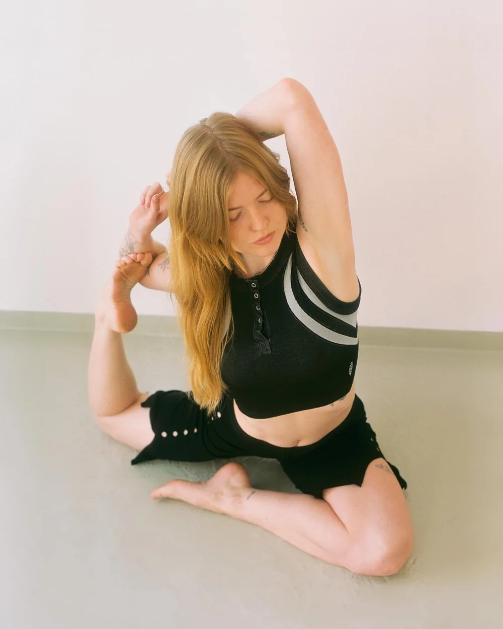 SVERA studio photography: a figure seated on the floor in a bound pose against a bare wall